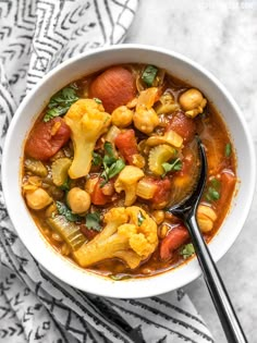 a white bowl filled with vegetable stew on top of a black and white towel next to a spoon