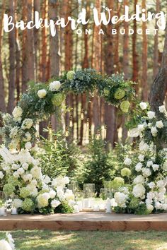 an outdoor wedding setup with white flowers and greenery on the table, surrounded by tall trees