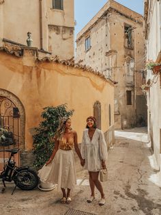 two women holding hands and walking down an alleyway in the old part of town