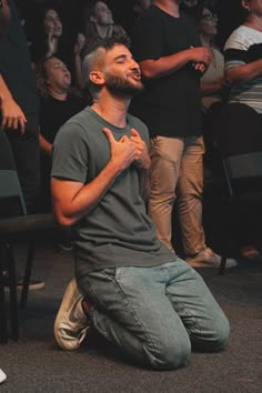 a man sitting on the ground in front of a crowd with his hands clasped to his chest