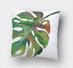 a cross stitch pillow with a green plant on it