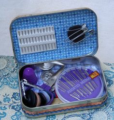 an open suitcase filled with lots of crafting supplies on top of a blue and white tablecloth