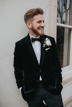 a man in a tuxedo standing next to a window smiling at the camera