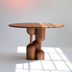 a round wooden table with three legs and a light shining on the wall behind it