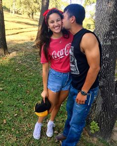 a man and woman are kissing in the grass next to a tree with their feet on each other