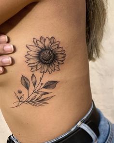 a sunflower tattoo on the side of a woman's rib - up stomach