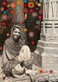 a woman sitting on the ground in front of a building with many colorful decorations hanging from it