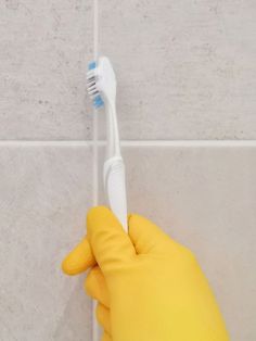 a person in yellow gloves holding a toothbrush up to the side of a wall