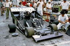 a man sitting on the ground next to a race car with an engine in it