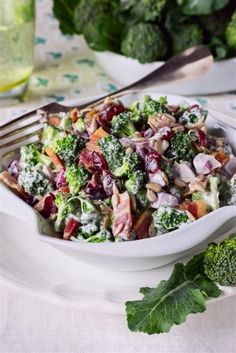 a salad with broccoli and cranberries in a white bowl on a table