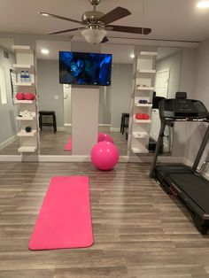 a room with exercise equipment and a television in the corner, including a pink yoga mat