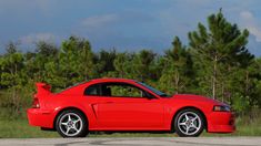 a red sports car is parked on the side of the road in front of some pine trees