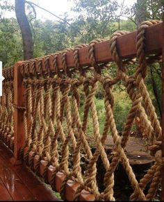 a wooden bridge with rope hanging from it's sides and trees in the background