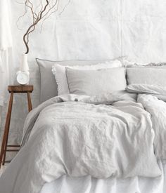 a bed with white linens and pillows in a room next to a tree branch