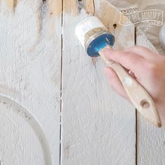 a person painting the side of a wooden wall with white paint and a blue brush