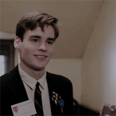 a young man in a suit and tie smiles at the camera while wearing a badge