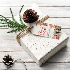 a present wrapped in white paper and tied with twine, next to a pine cone