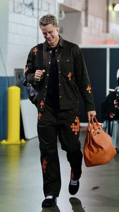 a man with a handbag is walking down the street while wearing black and orange