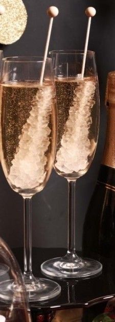 two champagne flutes filled with sparkling liquid and topped with wooden straws next to a bottle of champagne