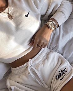 a woman laying on top of a bed wearing white sweatpants and a nike watch