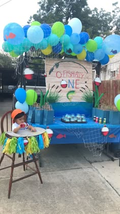 a little boy sitting in a high chair at a birthday party with balloons and decorations