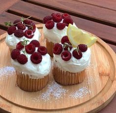 two cupcakes with white frosting and raspberries on top are sitting on a wooden plate