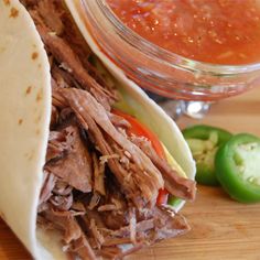 a close up of a taco with meat and vegetables on a cutting board next to a bowl of sauce