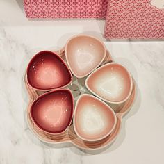 six pink bowls are arranged in a circle on a marble countertop next to a red box