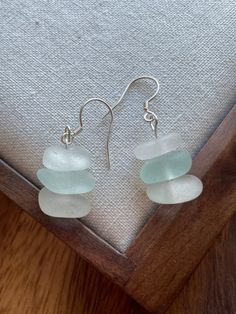 sea glass and sterling earwires are displayed on a piece of fabric in front of a wooden frame