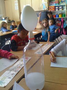 children are sitting at desks in a classroom with water and paper on the table