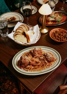 a wooden table topped with plates of pasta and bread next to glasses of red wine