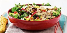 a red bowl filled with chicken salad next to an open baguette on a white table