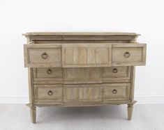 an old wooden dresser with many drawers and knobs on the bottom drawer, against a white wall