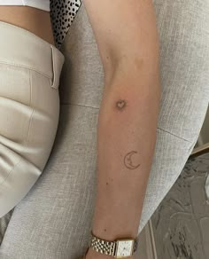 a woman's arm with a small sun and moon tattoo on her left arm