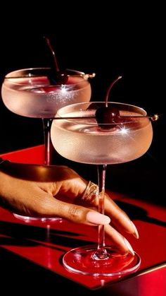 two martinis sitting on top of a red table with one being filled with liquid