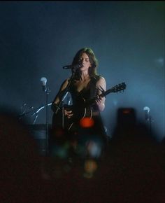 a woman holding a guitar while standing in front of microphones and singing on stage