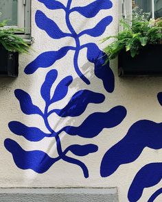 blue leaves painted on the side of a building with plants growing out of it's windows