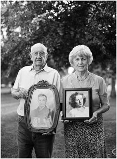 an older man and woman standing next to each other holding a framed photo in their hands