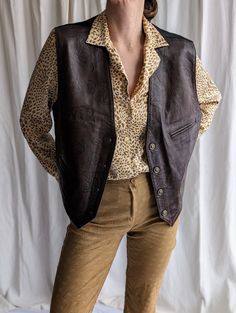 Stand out from the crowd in this vintage brown leather vest waistcoat made in Spain - a must-have addition to your wardrobe! This smart-casual style vest feature: . Gold tone buttons to exude old-school charm while looking effortlessly chic . Abstract pattern on brown leather fabric . 2 front pockets for functionality . Tie at back provides adjustable fit . Snap buttons for easy wear  . Casual smart look suitable for any occasion With its timeless design, this waistcoat vest elevates any outfit. Retro Fall Vest With Buttons, Vintage Fall Vest With Buttons, Vintage Workwear Vest With Buttons, Vintage Vest With Buttons For Workwear, Vintage Buttoned Vest For Workwear, Casual Brown Vest With Button Closure, Retro Workwear Vest With Button Closure, Vintage Workwear Vest Outerwear, Vintage Leather Vest Outerwear