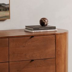 a wooden dresser with two books and a vase sitting on top of it next to a painting