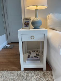 a small white table with a magazine on it next to a lamp and couch in the background