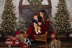 a woman sitting on a chair holding a baby in front of christmas trees and presents