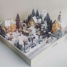 a christmas village is displayed in a box with lights and snow on the ground,