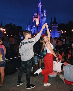 a man and woman dancing in front of a castle at night with their hands up