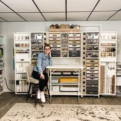 a woman sitting on a chair in front of a desk with lots of drawers and shelves