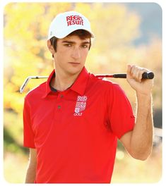 a man holding a golf club in his right hand and wearing a red polo shirt