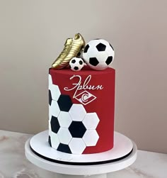 a red and white cake with soccer balls on top is sitting on a table in front of a wall