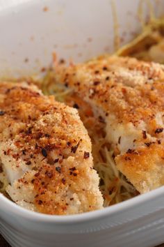 a white dish filled with chicken covered in grated cheese and seasoning sprinkles