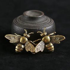 two gold bee brooches sitting next to each other on a black cloth background