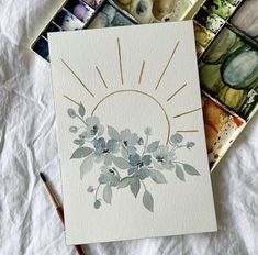 a card with watercolors and an artist's palette on the table next to it